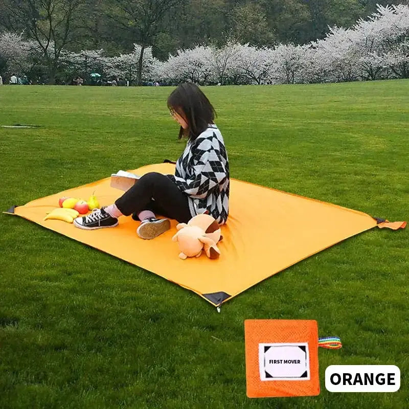 Femme assise sur un mat de camping portable orange dans un parc, idéal pour des pique-niques, des sorties à la plage, des moments de détente dans la nature, des festivals ou des randonnées.