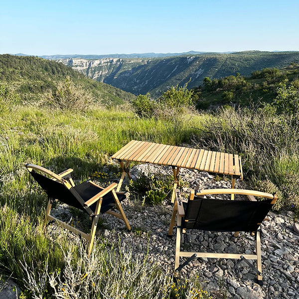 Chaises de camping en bois pliantes noires avec table installées dans un paysage montagnard pittoresque pour se détendre en plein air.