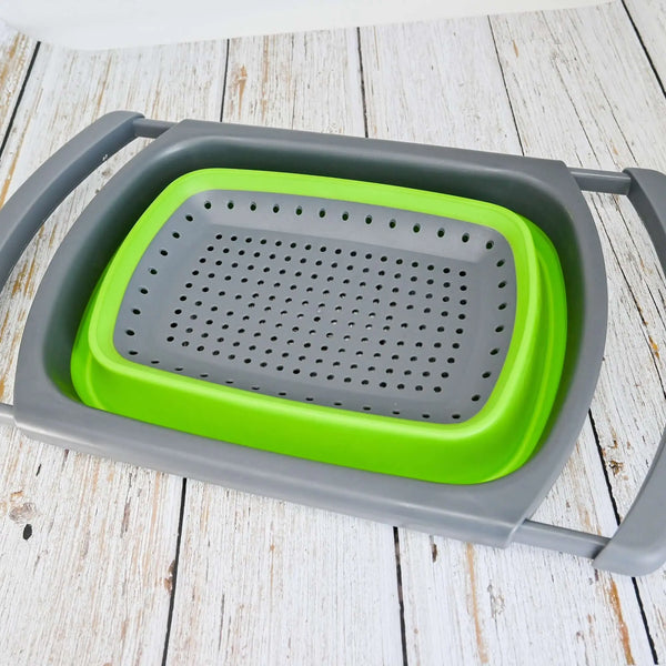 Passoire pliable en silicone verte avec poignées réglables, idéale pour le camping et les voyages, posée sur une table en bois.