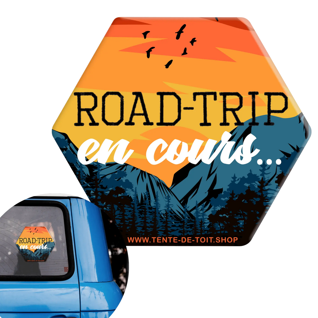 Autocollant de voiture "Road-Trip en cours" avec montagnes et coucher de soleil pour vanlife, fixé sur une fenêtre de voiture bleue.