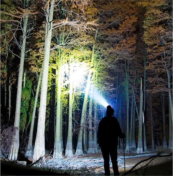 Une personne utilisant une lampe frontale haute puissance pour éclairer une forêt la nuit, montrant la luminosité de 90 000 lumens de la lampe pour les activités en plein air.