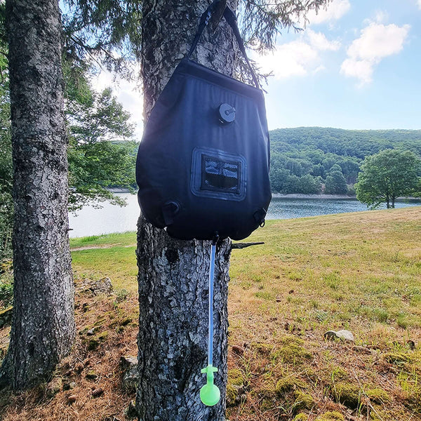 Poche de douche solaire de 20L accrochée à un arbre, idéale pour le camping sauvage en pleine nature, chauffée par l'énergie solaire.